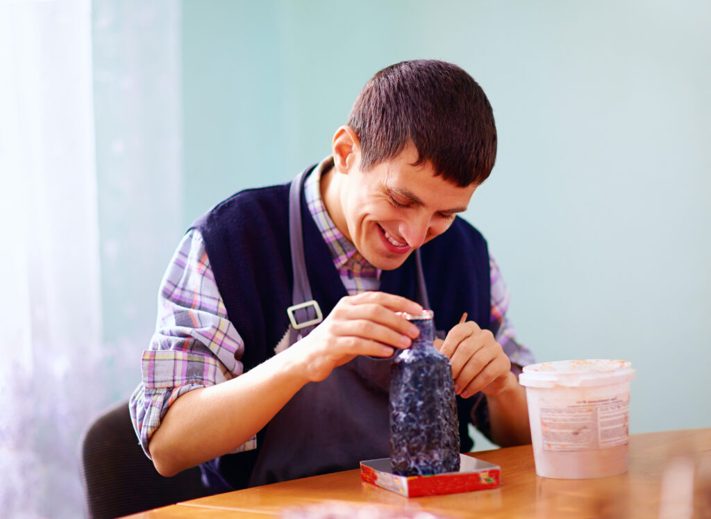 Young adult with special needs painting pottery with JSSA's Out and About social club