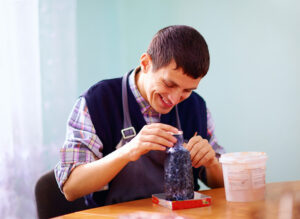 Young adult with special needs painting pottery with JSSA's Out and About social club