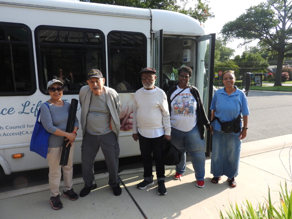 group of older adults pose beside a white bus