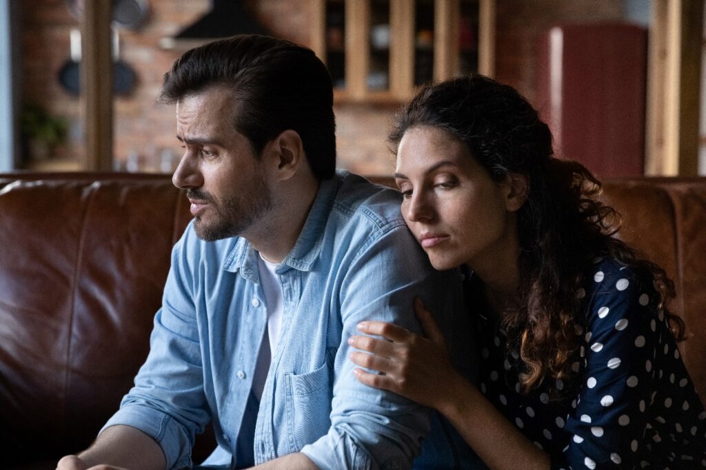 Woman leaning on the shoulder of a man for support. She has a sorrowful expression.