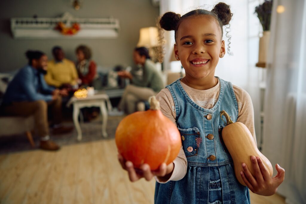 young girl smiling and holding pumpkins in front of a celebratory gathering