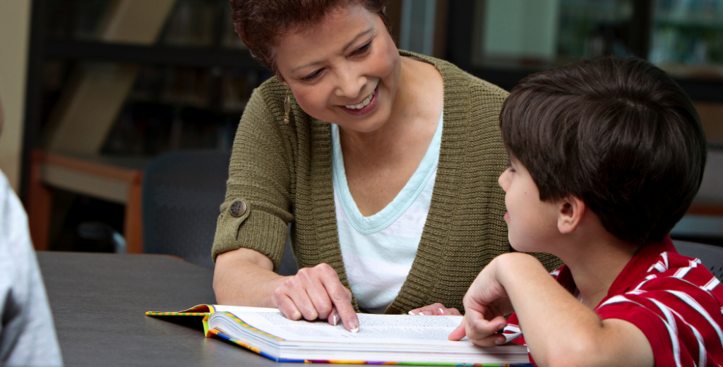 woman helps young boy read from a book